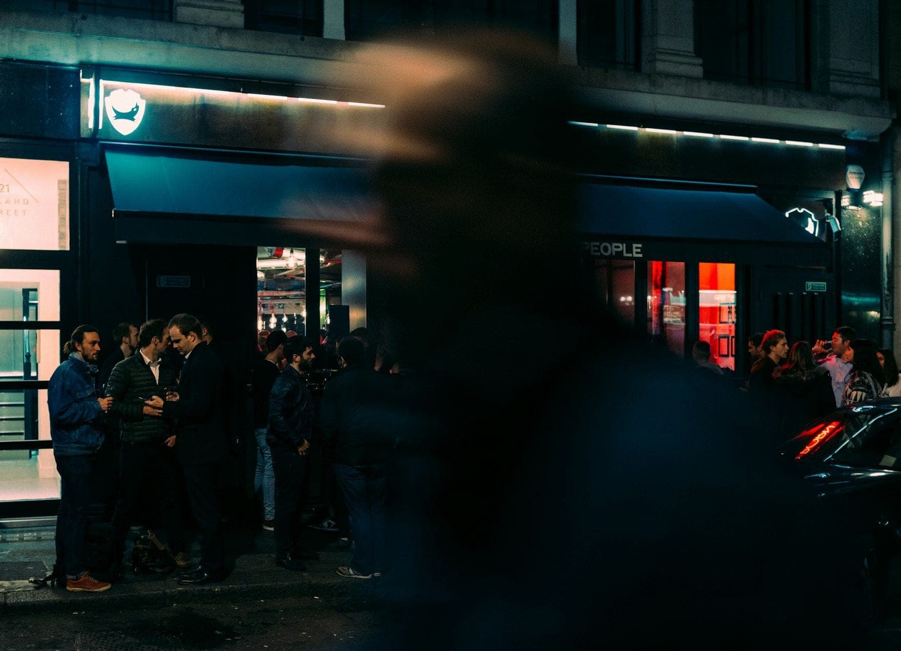 A bar front at night with customers queuing outside
