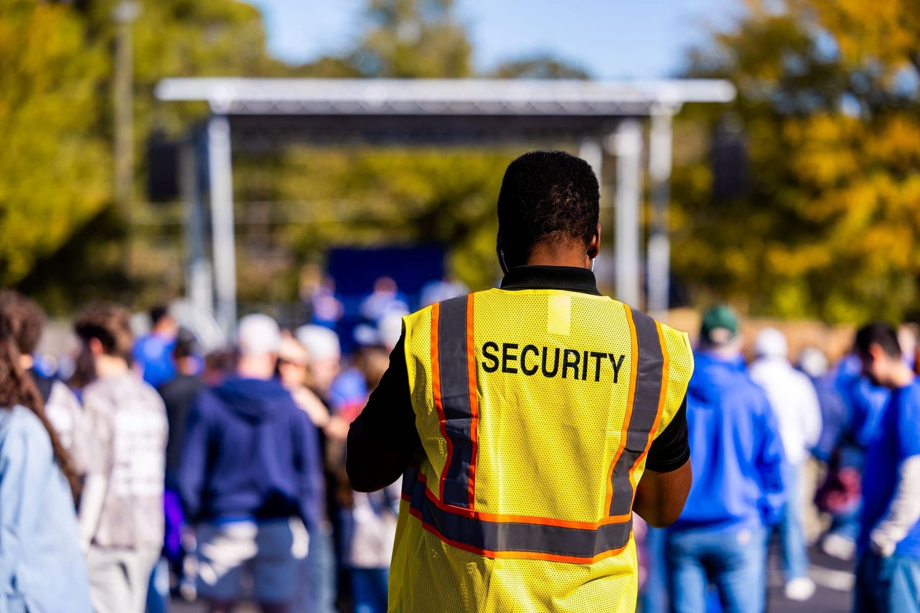 Security officer in a hi-vis vest facing an outdoor crowd at a stage